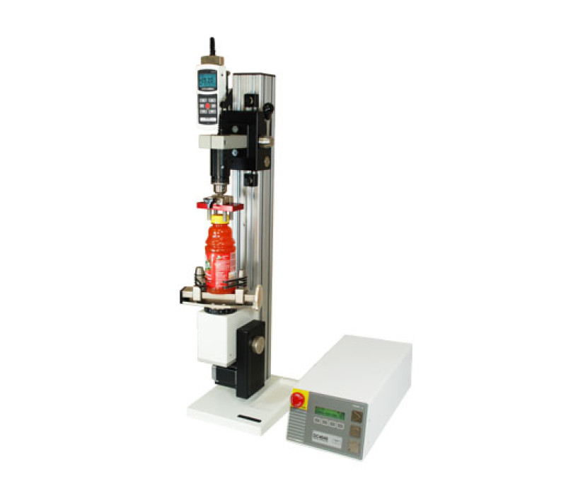 El banco de pruebas de par motorizado avanzado vertical TSTM-DC se muestra en una aplicación típica de pruebas de par de tapón de botella con indicador de fuerza/par 5i, sensor de par de la serie R50 y mordazas.